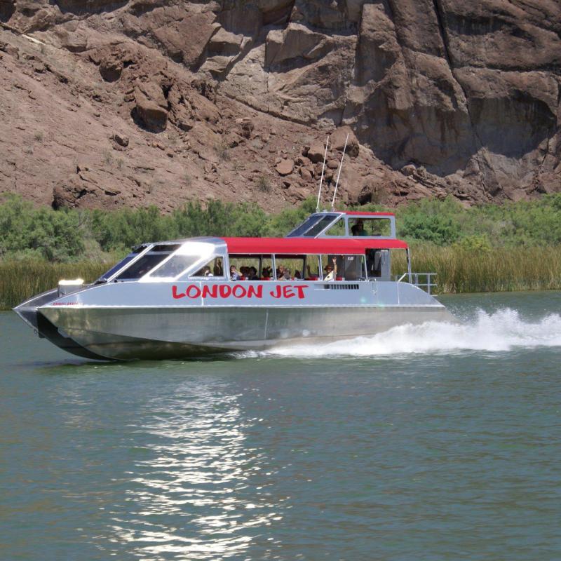 Jet boat named 'London Jet' speeding on a river with rocky cliffs and greenery in the background.