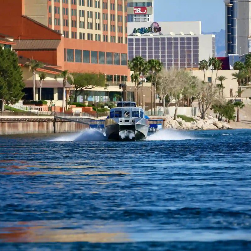 Boat speeding on a river with buildings and palm trees in the background.