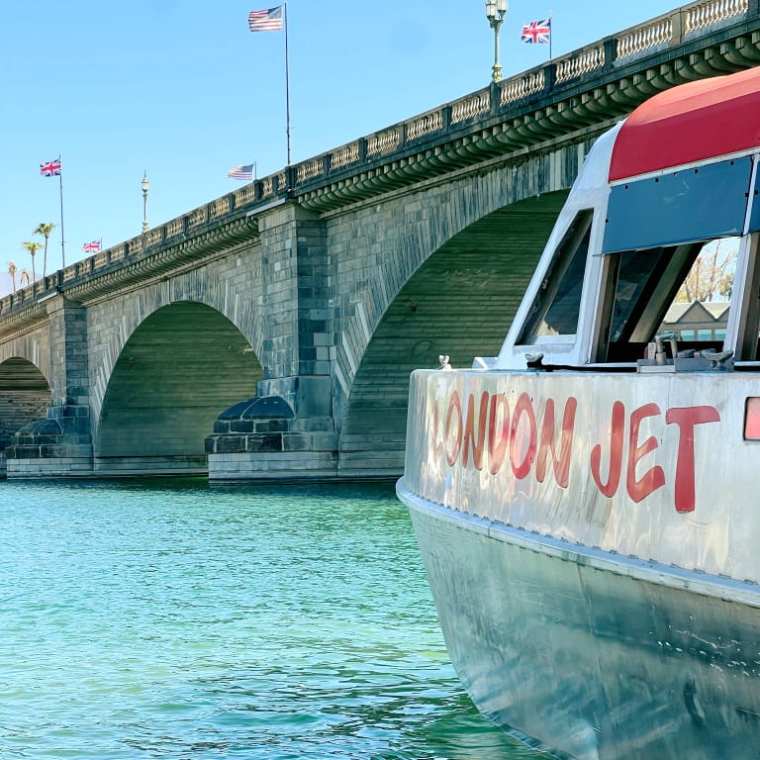 A jet boat near a stone bridge with flags in the background on a clear day.