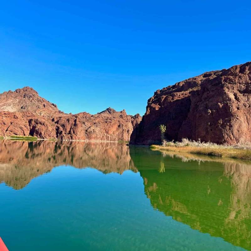 Clear blue sky over rocky desert landscape with still green water reflection.