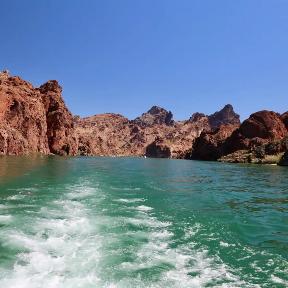 Clear river flowing between red rocky cliffs under a bright blue sky.