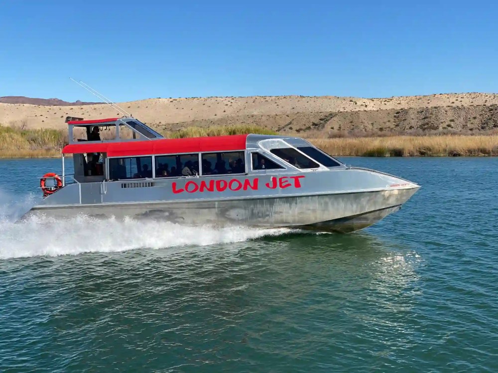 Silver jet boat with red roof labeled 'London Jet' cruising on a river.