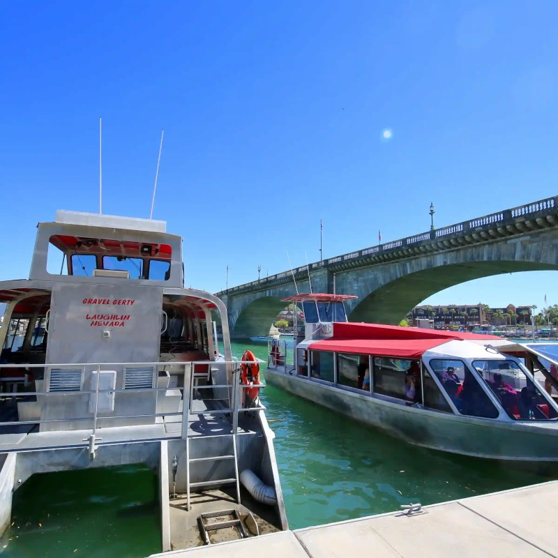 Two boats docked by a bridge over green water on a sunny day.