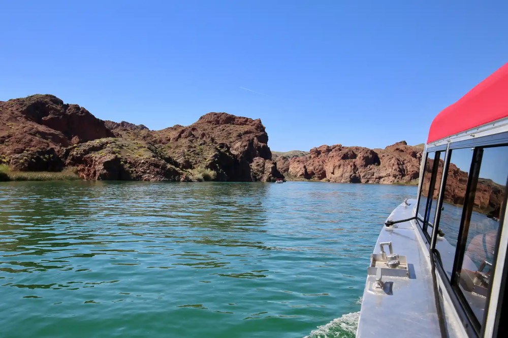 Boat on a lake with rocky desert cliffs under clear blue sky.