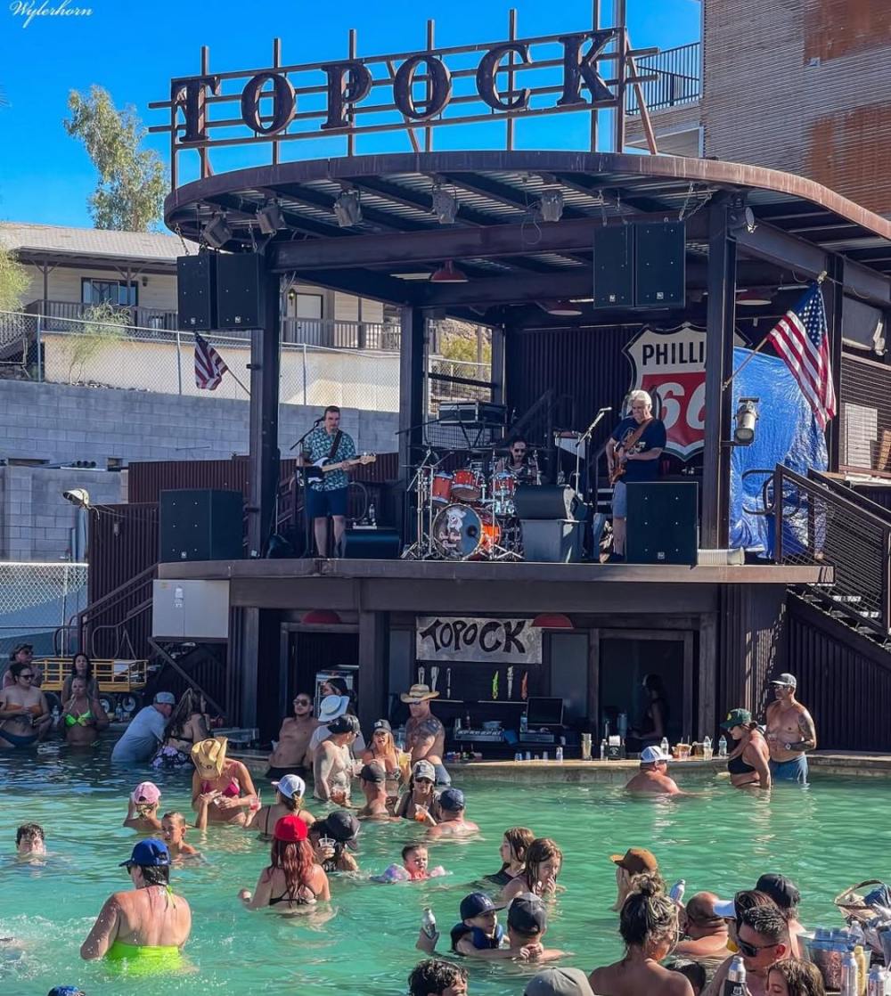 People in a pool listening to a live band playing on a deck labeled 'Topock' with American flags around.