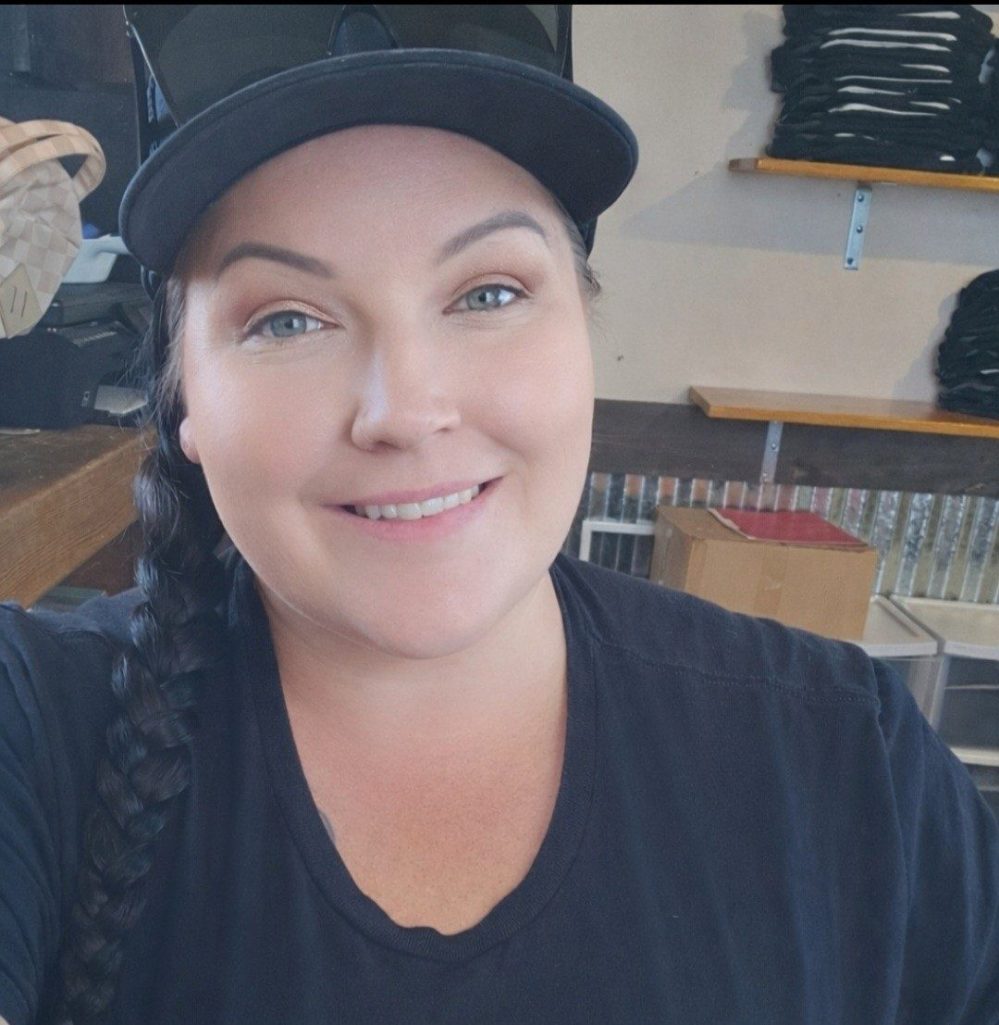 Smiling person with a braid and cap in a casual setting.